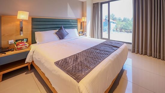 Bedroom with double size bed, bedside lamp on either side, and a balcony  attached - Pride Resort Ambaji
